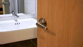 banheiro porta alças, porta com inoxidável botão porta metade aberto dentro frente do interior banheiro branco Pia do lavando mãos e espelho foto