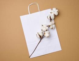 branco papel saco e uma ramo com algodão flores em uma luz Castanho fundo, zero desperdício foto