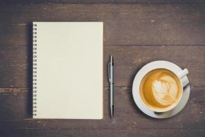 topo Visão caderno e caneta com café copo em madeira mesa, vintage filtro. foto