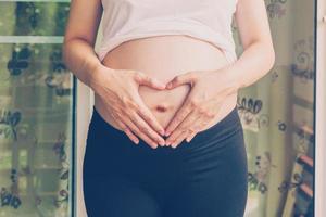 grávida mulher segurando mão coração forma para bebê dentro dela barriga foto