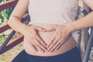 grávida mulher segurando mão coração forma para bebê dentro dela barriga foto