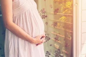 fechar acima mão grávida mulher segurando barriga com vintage tonificado foto