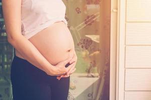fechar acima mão grávida mulher segurando barriga com vintage tonificado foto