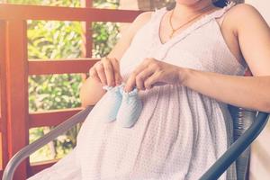 grávida mulher segurando pequeno bebê sapatos em dela barriga com vintage tonificado foto