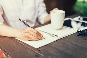 fêmea mão com lápis escrevendo em caderno. mulher mão com lápis escrevendo em caderno às café fazer compras. foto