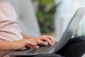 garotinha asiática da escola usa computador portátil sentado no sofá sozinho em casa. criança aprendendo lendo conteúdo de mídia social on-line, jogando lições de educação conversando com amigos. foto