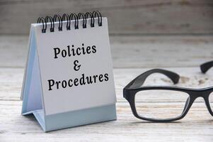 políticas e procedimentos texto em bloco de anotações com óculos em branco de madeira cobrir fundo. foto