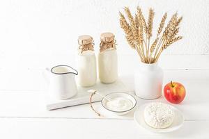 lindo festivo composição para a judaico feriado do shavuot. laticínios produtos em uma branco de madeira borda e uma vaso com pão ouvidos. branco fundo. foto