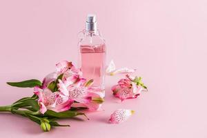 uma transparente perfume garrafa e a elegante composição com Primavera flores em uma Rosa fundo. frente visualizar. uma cópia de espaço. aroma apresentação. foto