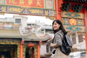 jovem ásia mulher mochila viajante desfrutando China Cidade rua Comida mercado dentro Bangkok, tailândia. viajante verificação Fora lado ruas. foto