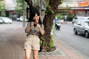 jovem ásia mulher mochila viajante usando digital compactar Câmera, desfrutando rua cultural local Lugar, colocar e sorriso. foto