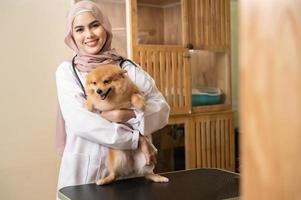 jovem fêmea muçulmano veterinário com estetoscópio examinando cachorro dentro veterinario clínica foto