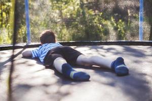 Garoto em a trampolim. a criança mentiras em uma trampolim e descansos foto