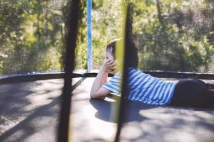 Garoto em a trampolim. a criança mentiras em uma trampolim e descansos foto