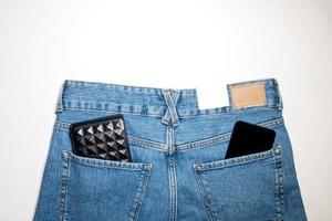 jeans calças com a esvaziar couro rótulo em uma azul fundo, carteira e telefone dentro a costas bolso foto