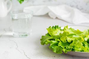 fresco alface folhas em uma prato e uma vidro do água em a mesa. saudável Comida em uma desintoxicação dieta. foto