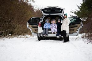 mãe com três crianças sentar em carro suv com aberto tronco ficar de pé dentro inverno floresta. foto