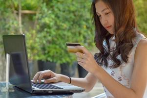 menina asiática segurando um cartão de crédito e usando laptop foto