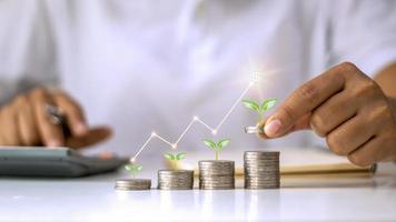 conceito de crescimento de investimento empresarial, uma pilha de moedas com uma pequena árvore crescendo em uma moeda e uma mão segurando uma moeda foto