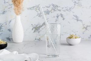 uma vidro do limpar \ limpo água e uma vidro Palha para bebendo em uma luz mesa. dieta orgânico estilo de vida foto