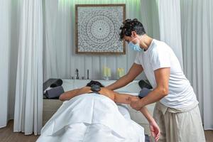 traseiro Visão do a adulto mulher tendo quente pedra massagem dentro spa salão enquanto obtendo a braço massagem foto