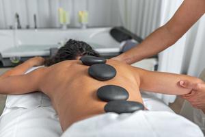 fechar traseiro Visão do uma mulher tendo quente pedra massagem dentro spa salão enquanto obtendo a braço e ombro massagem foto