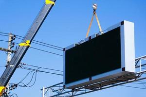 construção local guindaste é elevação uma conduziu tabuleta em branco Painel publicitário em azul céu fundo para Novo propaganda foto