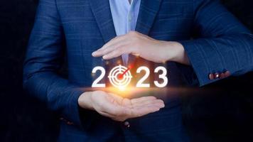 o negócio alvo e objetivo 2023 ícone, mão apontando segurando 2023 virtual tela, começar Novo ano 2023 com uma objetivo plano, açao plano, estratégia, Novo ano o negócio visão. foto