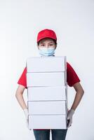 imagem de um jovem entregador consciente de boné vermelho camiseta em branco uniforme máscara facial luvas em pé com caixa de papelão branca vazia isolada no estúdio de fundo cinza claro foto