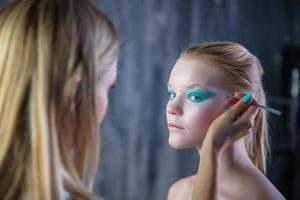 mulher aplica-se criativo Maquiagem para a face do uma adorável jovem modelo foto