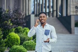 masculino aluna tendo Diversão falando em a telefone perto uma grande casa caminhando às hora do almoço foto