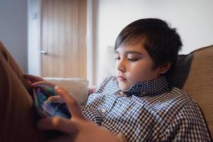 conceito de educação, garoto da escola segurando o tablet lendo e-book para lição de casa, retrato criança feliz jogando jogo online na internet com amigos, menino assistindo desenho animado no teclado digital, garoto sentado no sofá foto