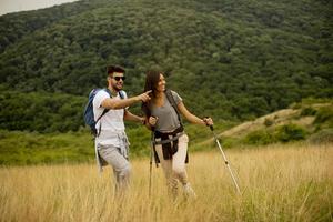 casal sorridente caminhando com mochilas pelas colinas verdes foto