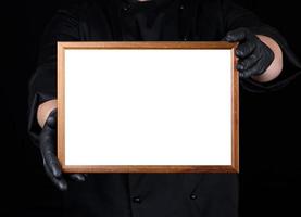 chefe de cozinha dentro Preto uniforme e Preto látex luvas segurando uma de madeira quadro, Armação com branco esvaziar espaço foto