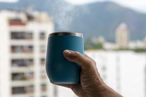 mão segurando uma caneca de café saindo da fumaça com fundo de ambiente urbano foto