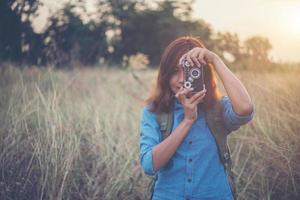 Mochileiro jovem hippie com uma câmera vintage em um campo foto