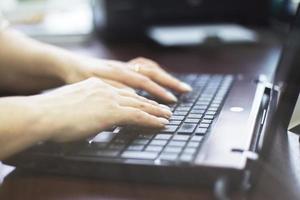 menina dentro a escritório é digitando em uma computador portátil. menina às trabalhar. menina mãos em teclado fechar foto