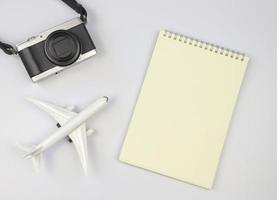 plano deitar do em branco página aberto caderno, avião modelo e Câmera em branco fundo com cópia de espaço. viagem, foto e memória conceito.