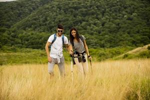 casal sorridente caminhando com mochilas pelas colinas verdes foto