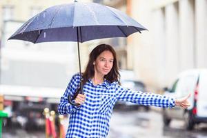 jovem mulher Perguntando para uma Táxi dentro a chuva foto