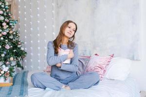 lindo jovem mulher posando dentro cama, cercado de Natal presentes, sentado foto