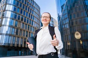 o negócio caucasiano mulher segurando uma computador portátil e ao ar livre cercado de edifícios. foto