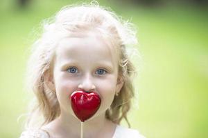 pequeno menina segurando uma pequeno vermelho coração. criança com uma brinquedo coração. foto