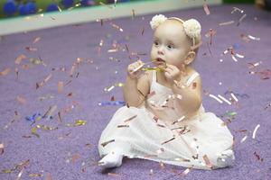 uma pequeno menina quem é 1 ano velho, senta em a chão dentro brilhante lantejoulas. foto