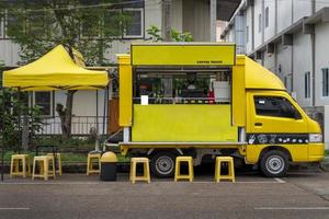 uma pequeno amarelo caminhão convertido para dentro uma Móvel café fazer compras com amarelo assentos e tendas servindo clientes. foto