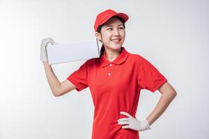 imagem do jovem entregador em uniforme de camiseta em branco de boné vermelho em pé com caixa de papelão branca vazia isolada no estúdio de fundo cinza claro foto