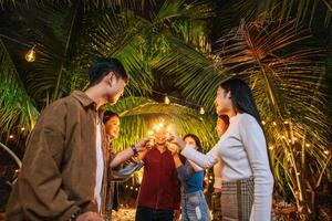 retrato de feliz grupo asiático de amigos se divertindo com estrelinhas ao ar livre - jovens se divertindo com fogos de artifício durante a noite - pessoas, comida, estilo de vida de bebida, conceito de celebração de ano novo. foto