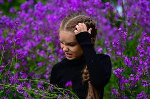 uma menina com grandes cabelo, caminhando dentro a campo. uma muitos do roxa flores ivan chá. foto tiro dentro natureza