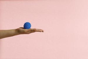 mulher mão com espinhoso plástico azul massagem bola em Rosa fundo foto