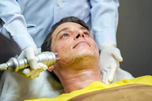 homem bonito closeup tendo terapia para estimular a pele facial e tratamento facial ultra-sônico pelo bem-estar cosmetologista profissional. foto